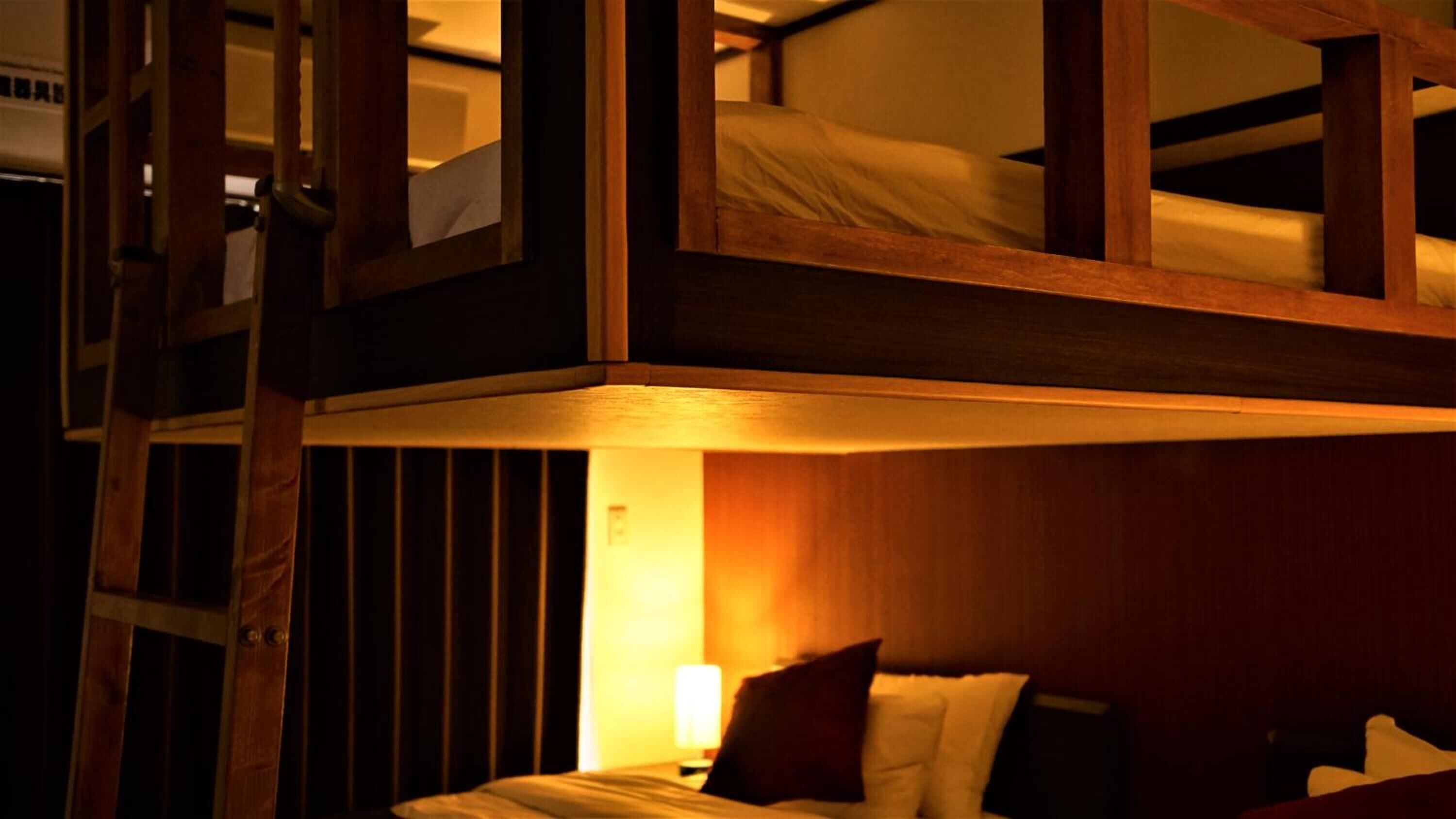 Habitación con literas, una escalera de madera, una mesita de noche con lámpara y una pared con rayas verticales.
