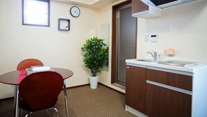 A small kitchen with a sink, a clock, a potted plant, and a dining area with a chair and table. - Hotel From Okinawa (Naha)