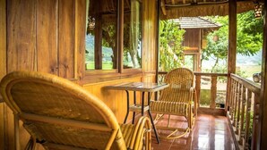 A wooden porch with wicker chairs and a glass table, overlooking a lush garden. - Mai Chau Nature Lodge - Hostel (Mai Chau)