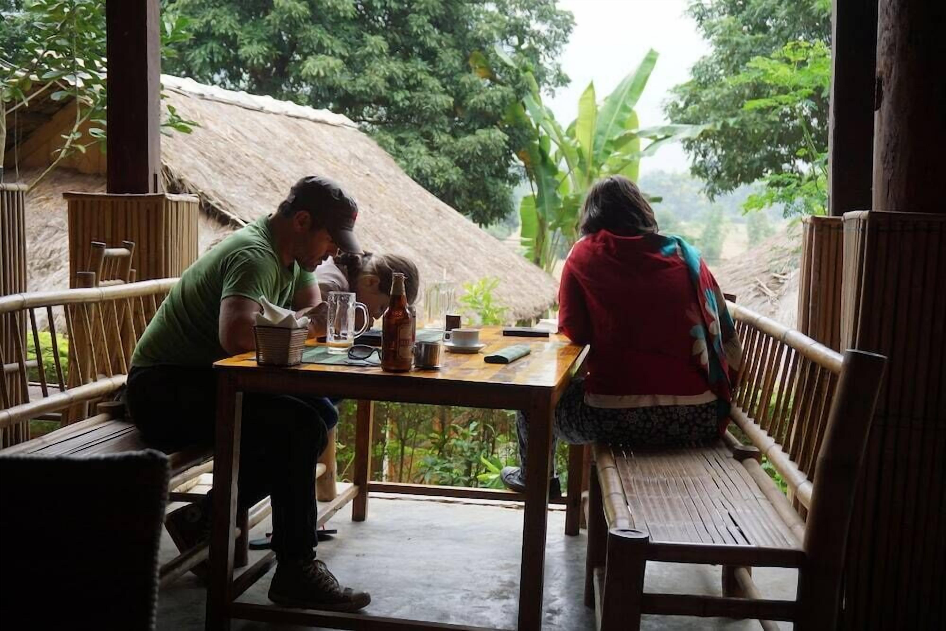 Two people seated at a wooden table with a thatched roof background.