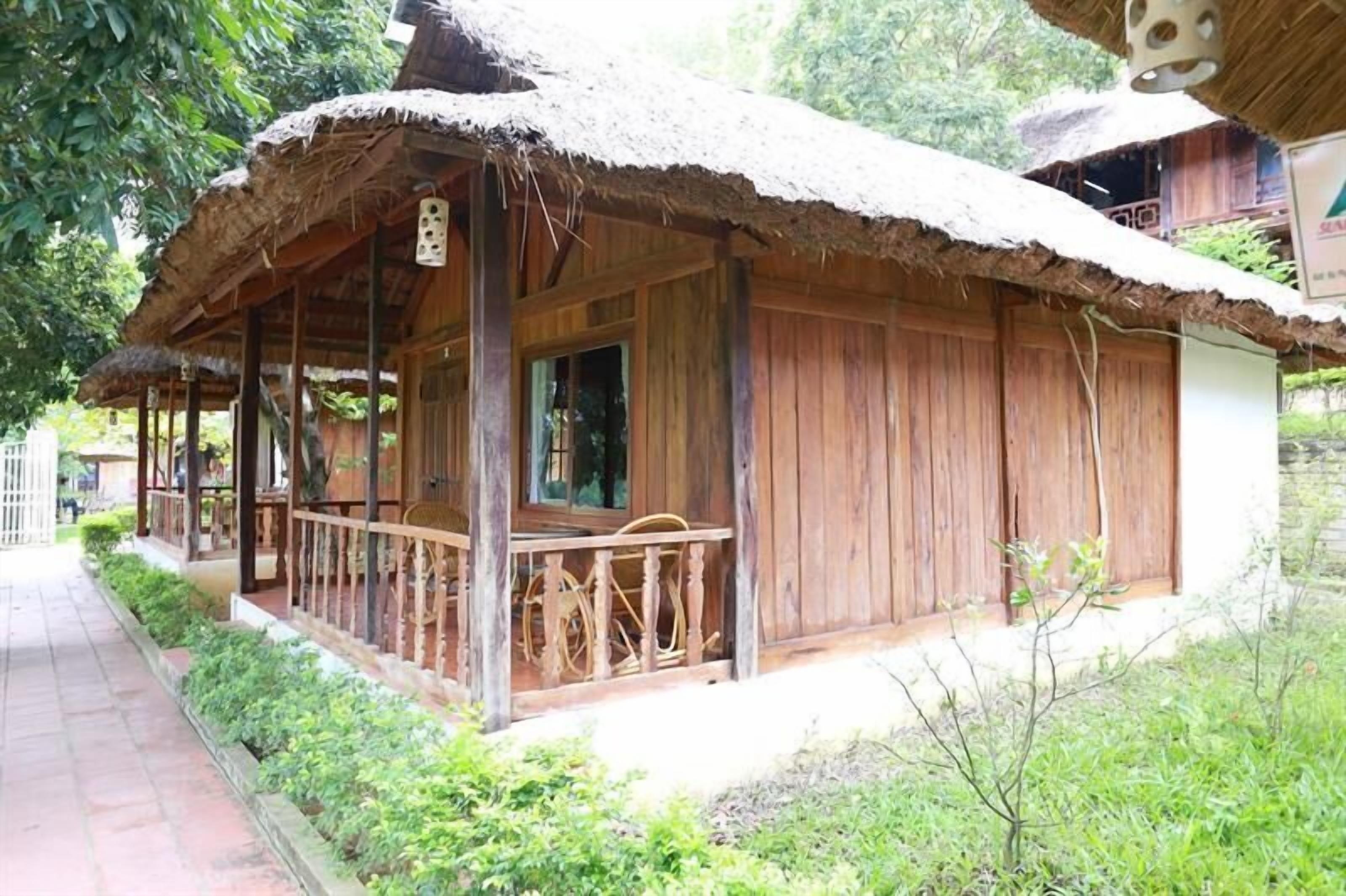 A wooden house with a thatched roof, a porch with a railing, and a window.