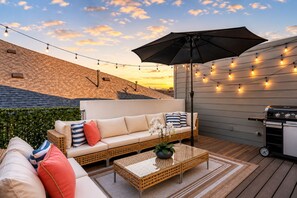 An outdoor patio with a sofa, a table, and string lights. - Double the Luxury: 8BR Duo, Sleeps 20, 2 Rooftops (HOUSTON)