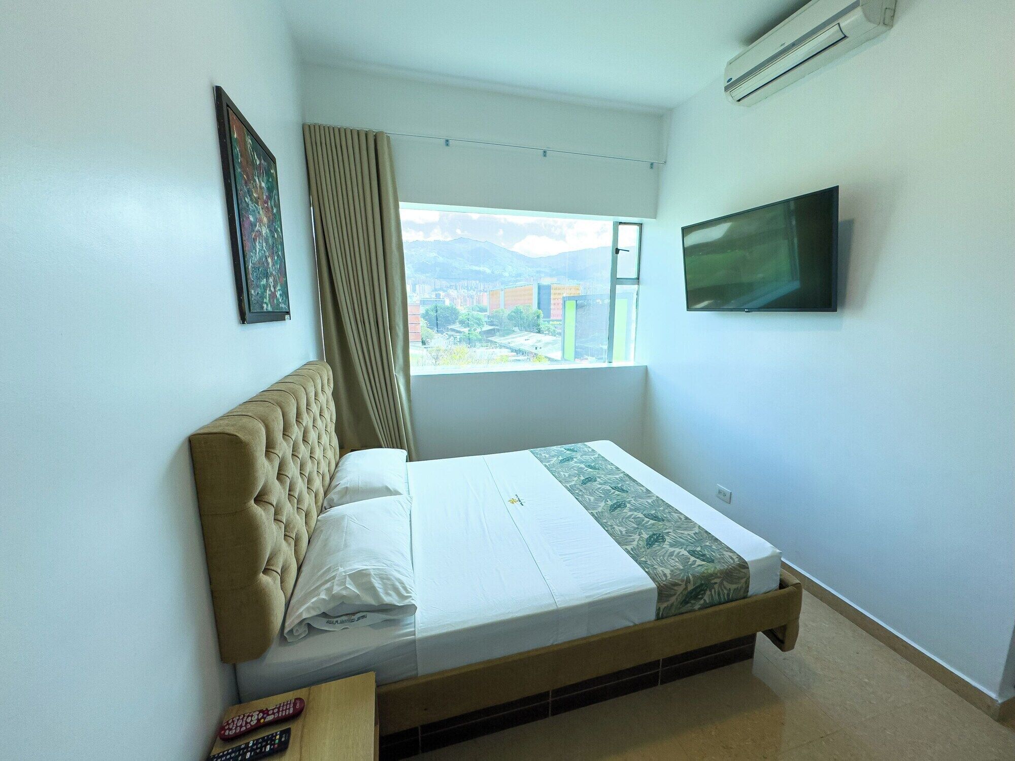 Una habitación de hotel con cama, ventana con vistas, televisor montado y aire acondicionado.
