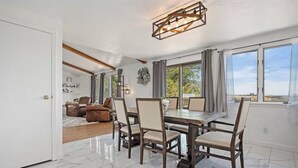 A dining area with a marble floor, wooden table, and chairs, a living room with leather sofas, and large windows with a view. - Rimview Haven: Hot Tub, Waterfall Trail & Golf! (Jerome)