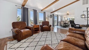 A spacious living room with leather sofas, a coffee table, and a view of the city through large windows. - Rimview Haven: Hot Tub, Waterfall Trail & Golf! (Jerome)