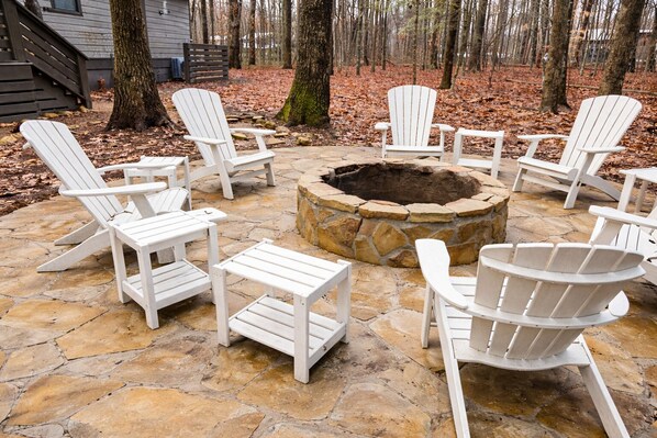 A stone patio with white Adirondack chairs arranged around a stone fire pit.