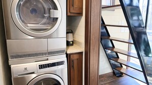 A compact laundry room with a front-loading washer and dryer, wooden cabinets, and a glass door leading to a staircase.