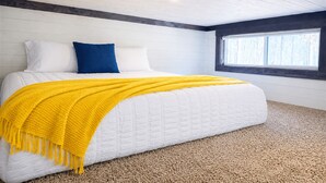 A bedroom with a bed, white walls, a window, and a yellow blanket.