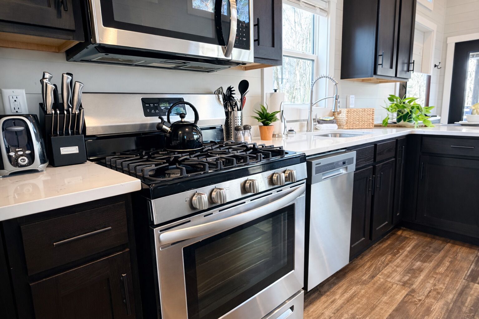 A modern kitchen with a gas stove, oven, microwave, and dishwasher. There are cabinets, a sink, and a window providing natural light.