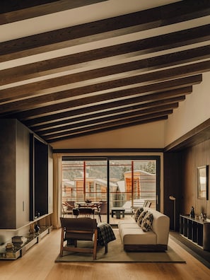 A modern living room with a wooden ceiling, large sliding glass doors to a deck, a sofa, and a dining area. - Campzero Active & Luxury Resort (Ayas)