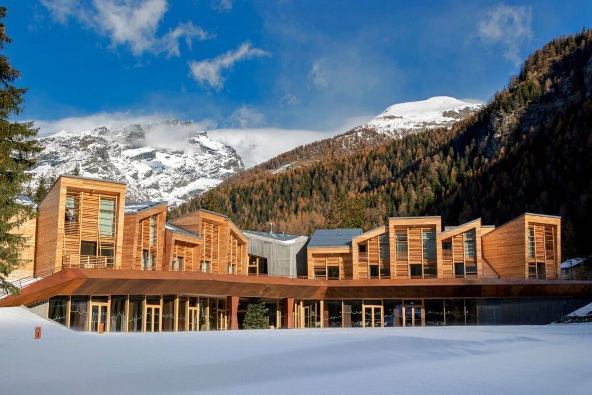 Un edificio moderno in legno con ampie finestre, sullo sfondo di una montagna innevata.