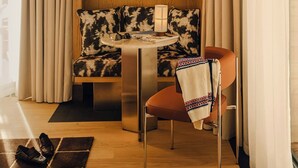 A modern room with a wooden accent wall, a sofa with patterned cushions, a table with a lamp, and a chair with a blanket. - Campzero Active & Luxury Resort (Ayas)