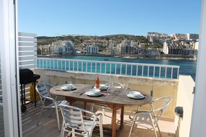 Un balcón con una mesa dispuesta para dos personas, con vista a un paisaje urbano costero.