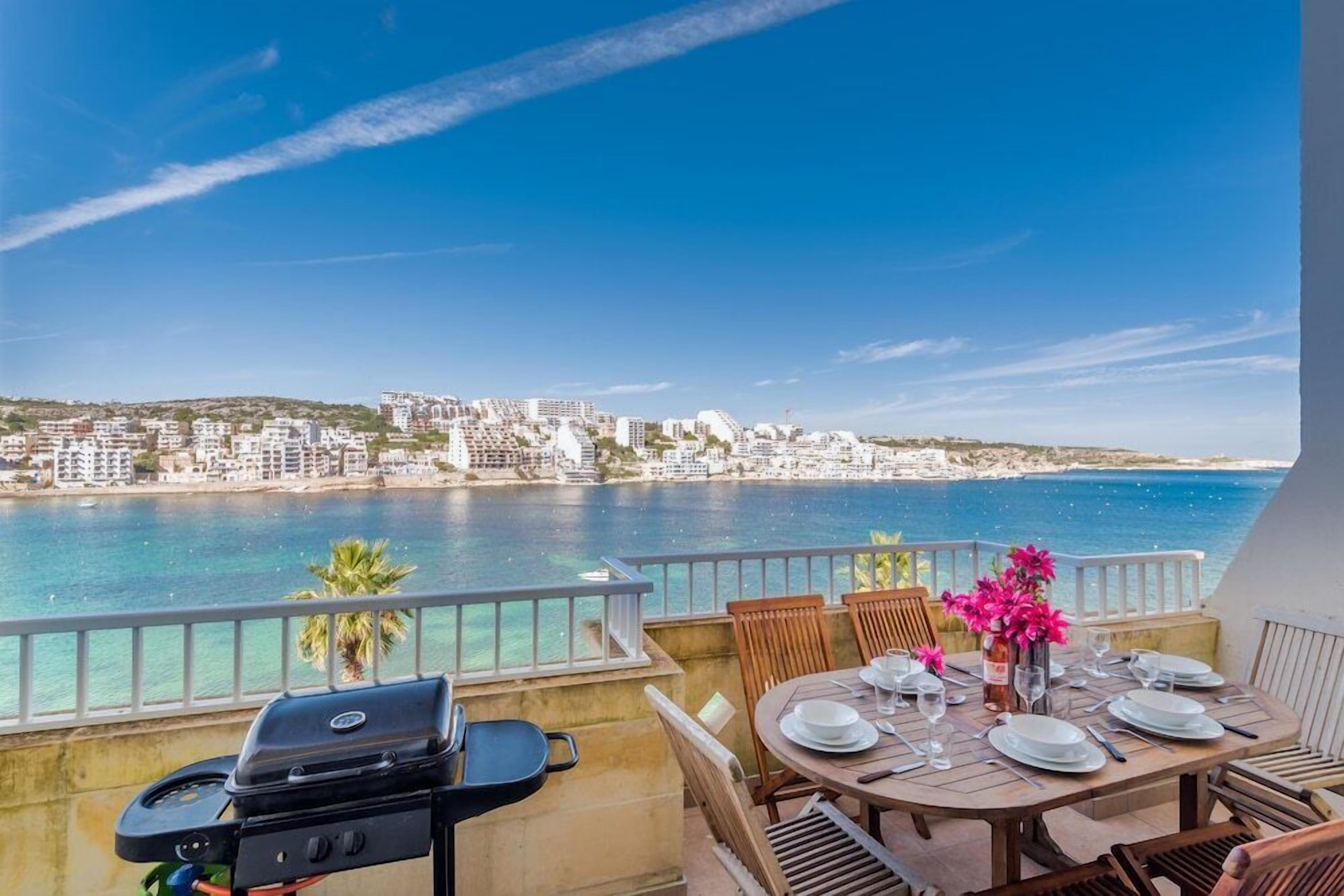 A balcony with a table set for dining, overlooking a coastal cityscape.