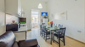 A modern kitchen with a microwave, toaster, and green appliances. There is a dining area with a table set for four, chairs, and a vase with flowers. A television is mounted on the wall. - Blue Harbour Penthouse (St. Paul's Bay)