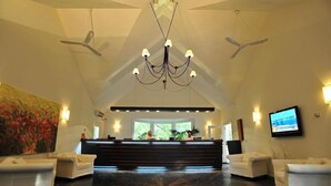 A hotel lobby with a reception desk, two white sofas, a chandelier, ceiling fans, and a television on the wall. - Solanas Punta Del Este Spa Resort (Punta del Este)