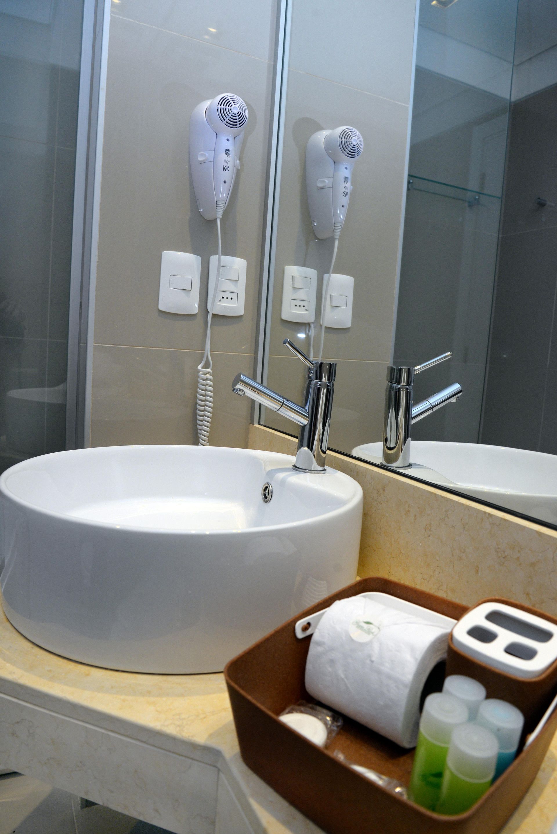 A bathroom with a large white sink, a mirror, and two hair dryers mounted on the wall.