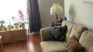 A living room with a sofa, a small table with a lamp, a floor lamp, and a window with curtains. - A cozy atmosphere and wonderful hosts make for a truly unforgettable experience. (Elliot Lake)