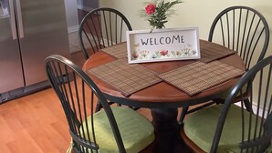 A dining area with a 'WELCOME' sign, chairs with cushions, a clock on the wall, and a kitchen in the background. - A cozy atmosphere and wonderful hosts make for a truly unforgettable experience. (Elliot Lake)