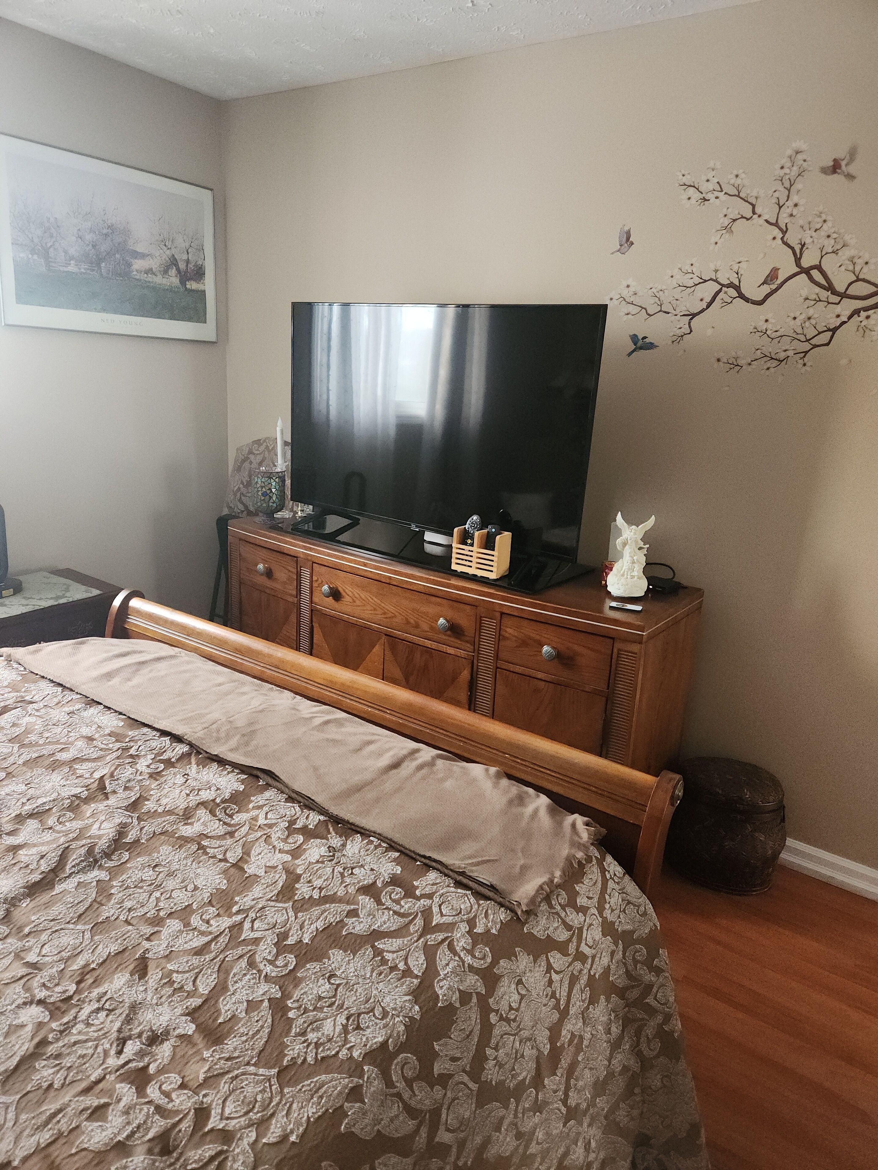 A bedroom with a bed, a wooden dresser, a television, and a wall decoration.