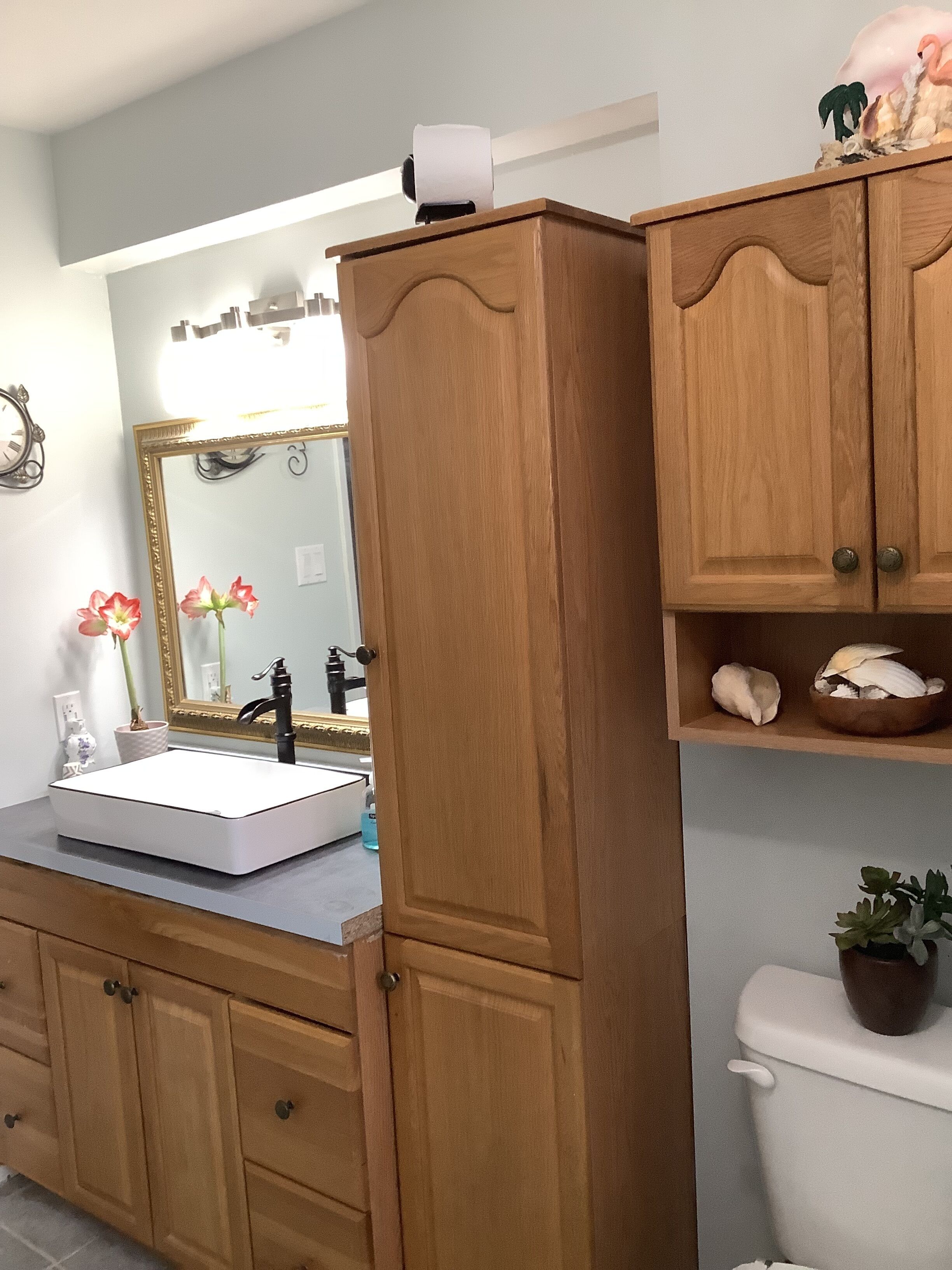 A bathroom with a wooden vanity, a white sink, a mirror, and a toilet.