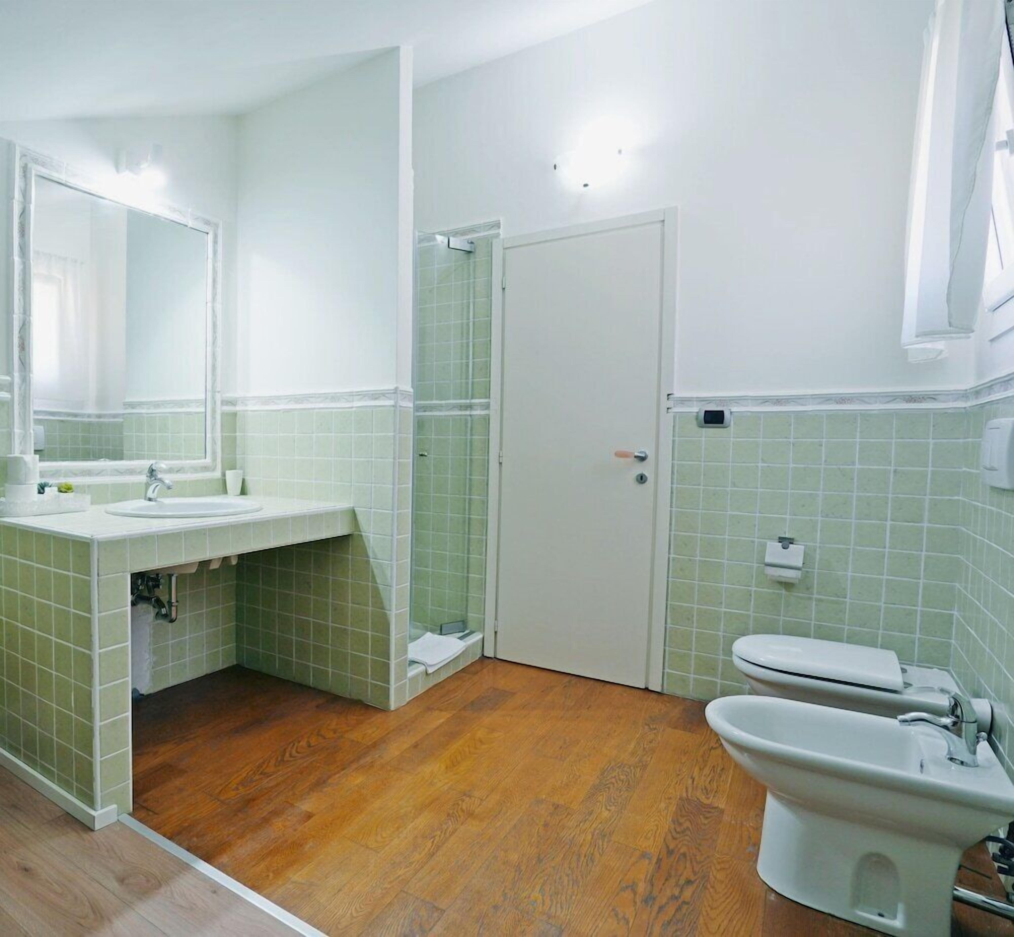 A bathroom with a sink, mirror, toilet, bidet, and a shower area.