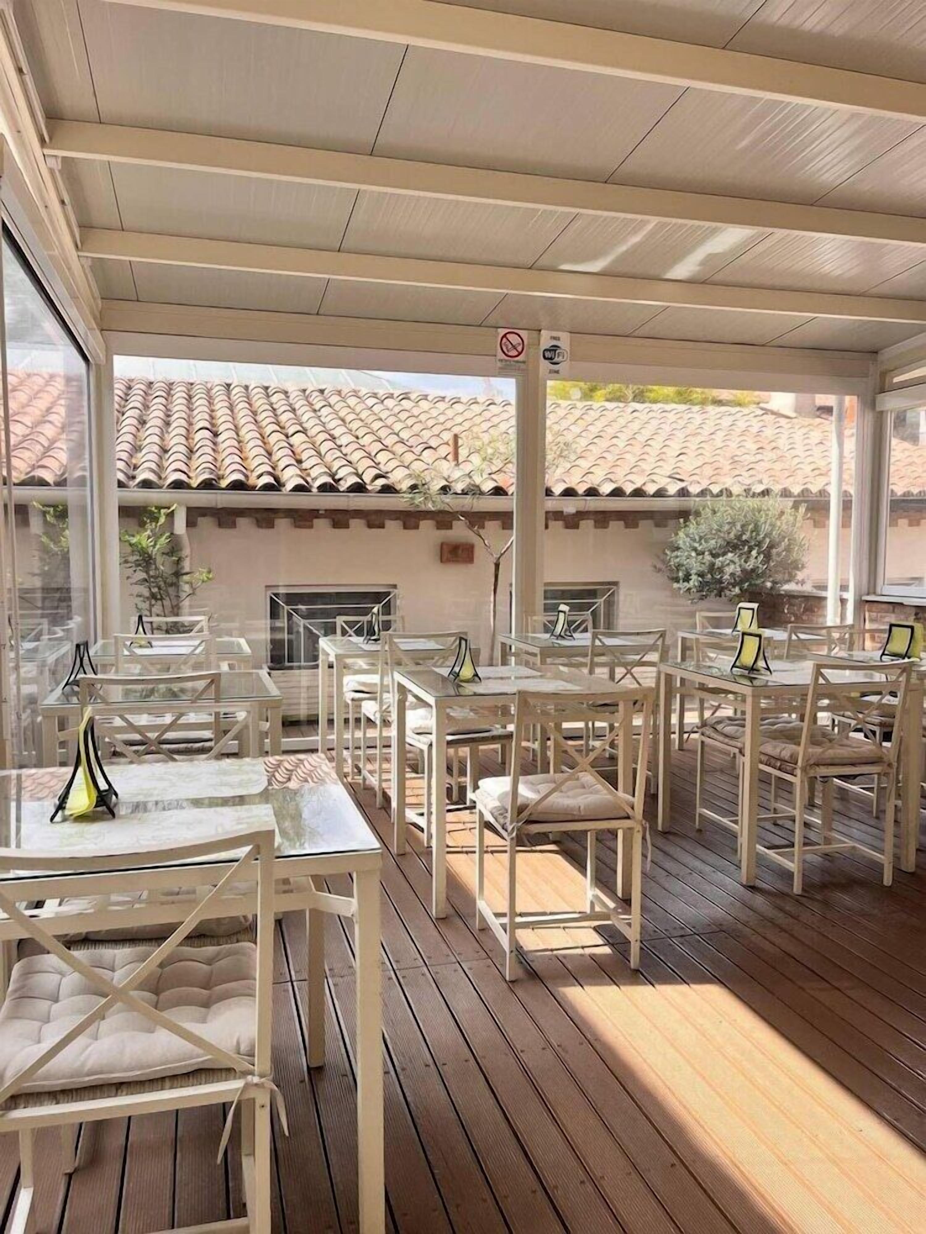 Un'area pranzo all'aperto con tavoli e sedie bianche, un tetto in tegole e vista su un edificio con tetto in tegole.
