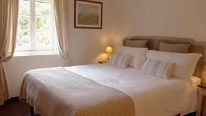 A neatly made bed with a white duvet and pillows, a bedside lamp, and a window with curtains. - Agriturismo Villanova (Levanto)