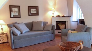 A living room with a grey sofa, a smaller armchair, a fireplace, and two framed pictures on the wall. - Agriturismo Villanova (Levanto)