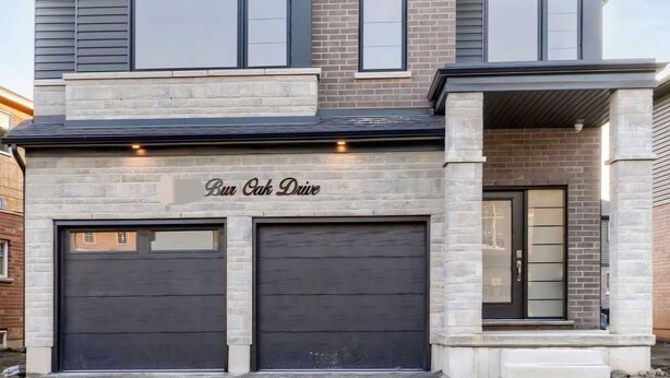 A two-story house with a garage, a covered porch, and a brick facade. - Niagara Cozzy Suite (Thorold)