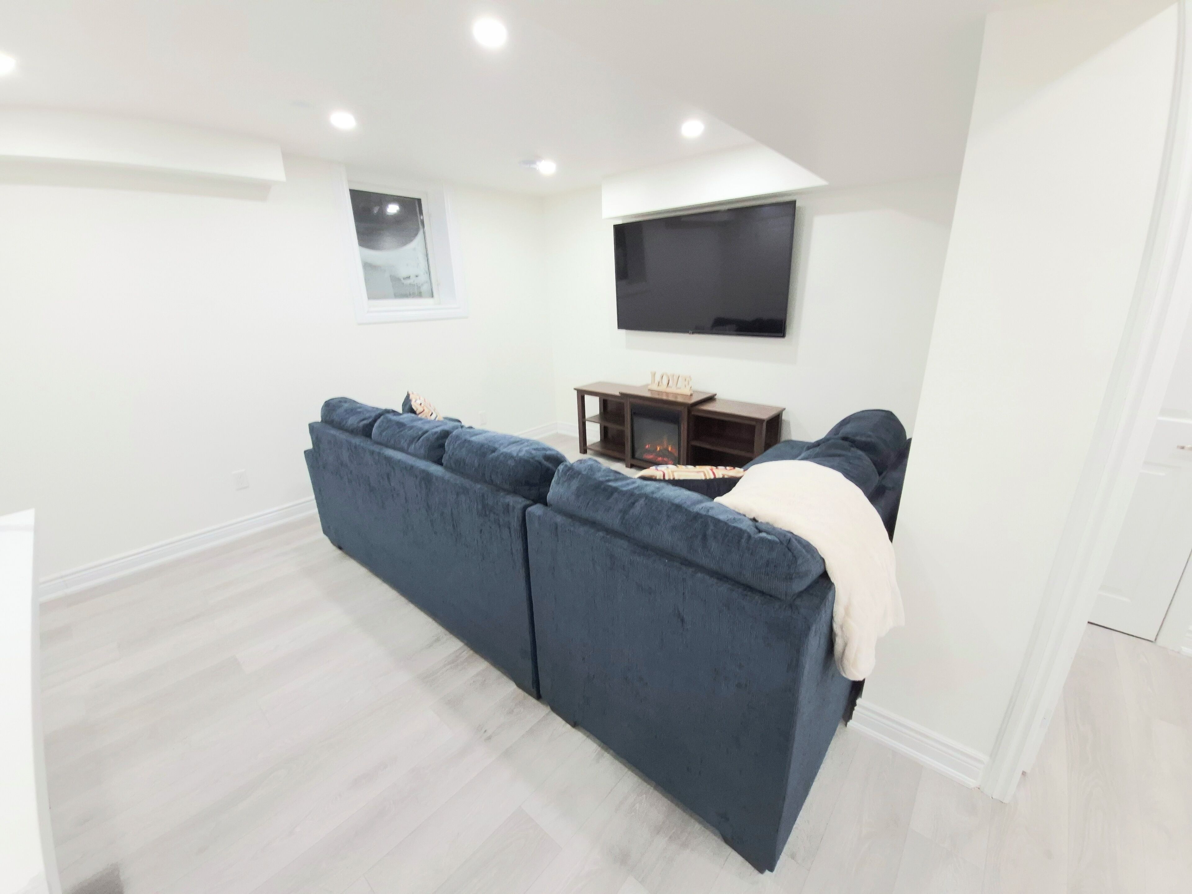 A modern living room with a dark blue sectional sofa, a flat-screen TV mounted on the wall, and a small wooden table with a fireplace.