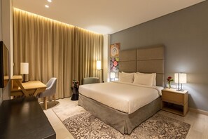 Hotelkamer met een groot bed, een bureau, een stoel, een nachtkastje met lampen en een decoratief wandobject.