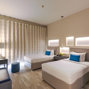 Ein Hotelzimmer mit zwei Betten, einem Schreibtisch, einem Stuhl, einer Lampe und einem Fenster mit Vorhängen.