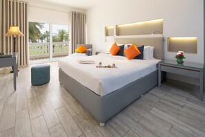 A modern hotel room with a large bed, a bedside table, a nightstand, a lamp, and a view of palm trees. - Sealine Beach, a Murwab Resort (Mesaieed)