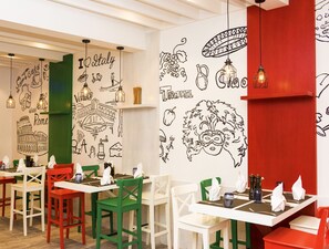 L’intérieur d’un restaurant, avec ses tables et ses chaises, est agrémenté d’œuvres d’art murales représentant des thèmes liés au voyage et à la gastronomie.