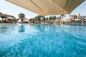Ein Schwimmbecken mit Liegestühlen und Sonnenschirmen, umgeben von Palmen und einem Gebäude.