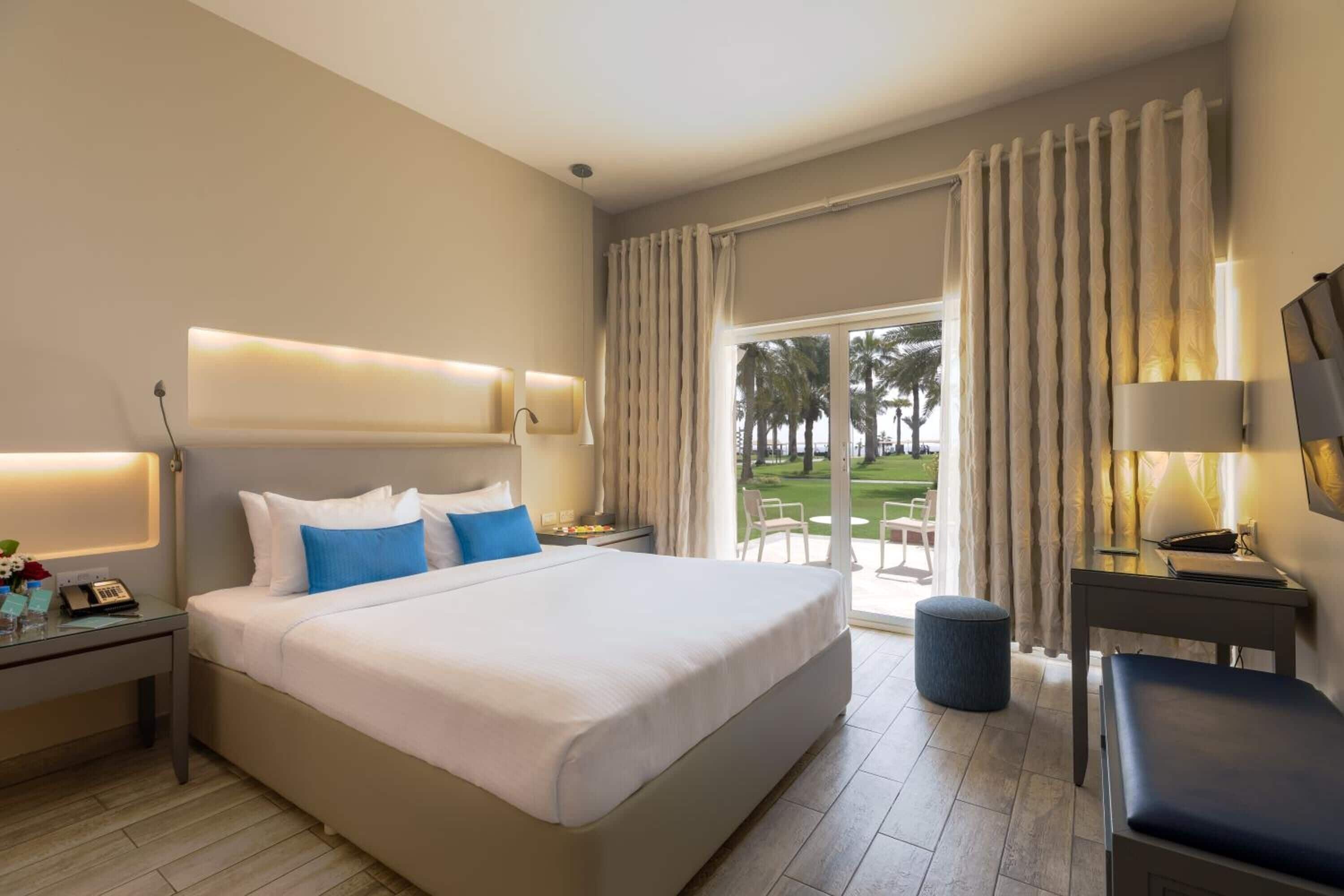 A hotel room with a large bed, bedside tables, a desk, and a view of the outdoors.