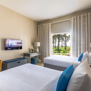 A hotel room with two beds, a desk with a lamp, a TV, and a view of palm trees. - Sealine Beach, a Murwab Resort (Mesaieed)