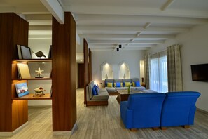 Ein modernes Wohnzimmer mit einem blauen Sofa, einem hölzernen Bücherregal und einem grauen Sofa mit blauen Kissen.