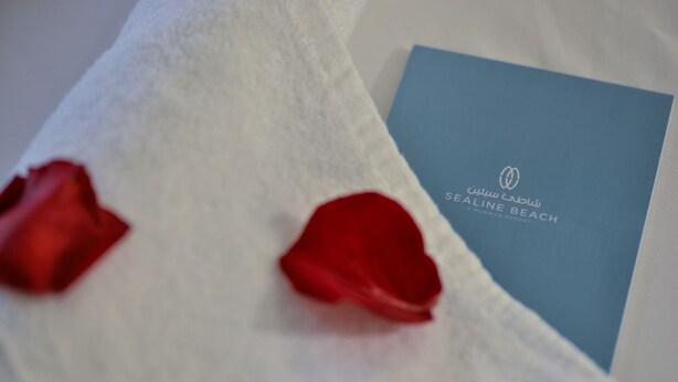 A blue booklet with "SEALINE BEACH" text and a logo, placed on a white surface with red rose petals. - Sealine Beach, a Murwab Resort (Mesaieed)