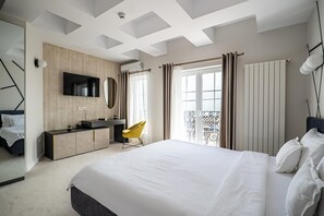 A modern hotel room with a large bed, a desk with a flat-screen TV, a mirror, and a balcony with curtains.