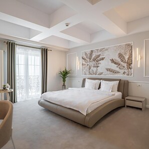 A modern bedroom with a large bed, a small bedside table, a potted plant, and a view of the balcony.