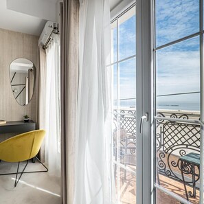 Una habitación con un ventanal grande, un sillón amarillo, un espejo redondo y una mesita pequeña.