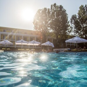 A swimming pool with umbrellas, a building in the background, and trees. - Central Mamaia (Constanta)