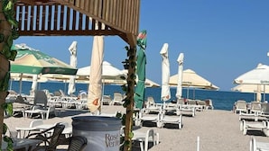 A beachside area with lounge chairs, umbrellas, and a wooden pergola structure. - Central Mamaia (Constanta)