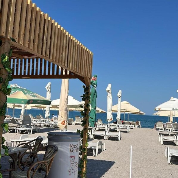 A beachside area with lounge chairs, umbrellas, and a wooden pergola structure. - Central Mamaia (Constanta)