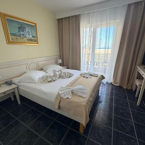 A hotel room with a bed, a nightstand, a desk, a chair, a window with curtains, and a painting on the wall. - Central Mamaia (Constanta)