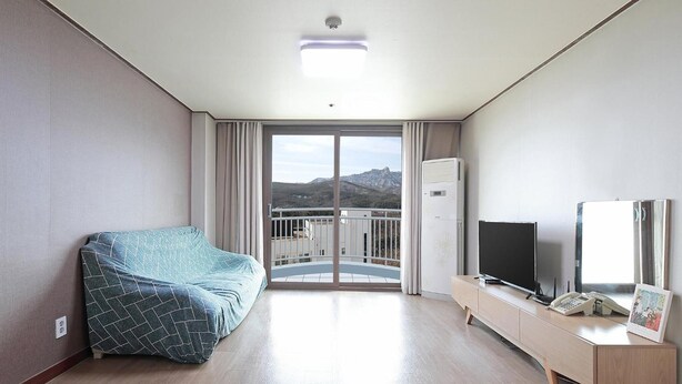 A modern hotel room with a balcony, a sofa, a TV, a bedside table, and a phone. - Ilsung Seorak Oncheo Condo and Resort (Goseong)