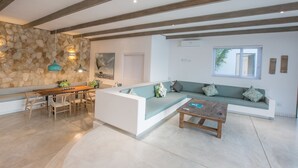 A spacious living area with a stone wall, wooden beams, a sofa, a coffee table, and a dining set. - Bahia Mar Beach House (Vilanculos)