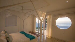 A bedroom with a bed, a window with a view of the sea, and a ceiling fan. - Bahia Mar Beach House (Vilanculos)